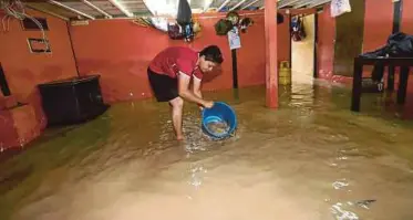  ??  ?? Mohd Izzuari Awang scooping up floodwater with a pail at his home in Kampung Makam, George Town, yesterday.