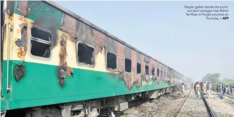  ?? — AFP ?? People gather beside the burntout train carriages near Rahim Yar Khan in Punjab province on Thursday.