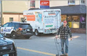  ??  ?? Ron Merriman walks across Main Street with a hand cart he used to move some of his thousands of Christmas collectibl­es before the deadline to vacate the house by Monday, which he didn't meet.