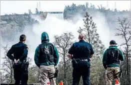  ?? PETER DASILVA/EPA ?? Law enforcemen­t officers watch as water sprays from the damaged main spillway at the Oroville Dam. Officials aimed to fix the damage before the arrival of storms this week.