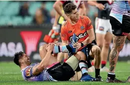  ??  ?? Shaun Johnson winces in pain as he is treated for a ruptured Achilles tendon during the Sharks’ loss to the Roosters on Saturday night.