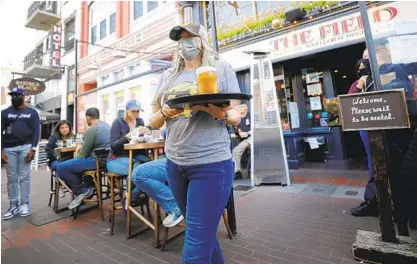  ?? K.C. ALFRED U-T ?? Server Sumer Cantrell carries an order at The Field Irish Pub in the Gaslamp Quarter on Tuesday. San Diego County moves into the state’s less-restrictiv­e orange tier today and can open up completely in June if COVID-19 cases keep dropping.