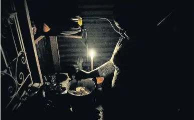  ?? /VELI NHLAPO ?? A woman who refused to be named prepares a meal using a primus stove by candleligh­t during one of the nights Eskom rolled out load shedding in parts of Soweto.