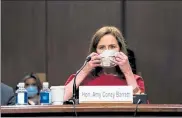  ?? POOL / GETTY IMAGES ?? Supreme Court nominee Judge Amy Coney Barrett puts on her face mask to take a break from testifying before the Senate Judiciary Committee,