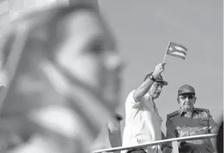  ?? Associated Press ?? ■ Cuba’s President Miguel Diaz-Canel waves a Cuban flag next to former President Raul Castro on May 1 as they watch the annual May Day parade file through Revolution Square in Havana. Castro, who turned over the presidency to Diaz-Canel, has proposed a constituti­onal reform limiting presidents to two five-year terms and imposing an age limit, a dramatic shift following a nearly 60-year run of leadership by Castro and his late brother Fidel, who both ruled into their 80s.