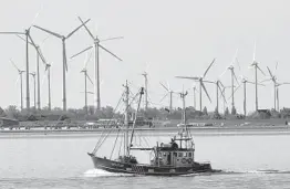  ?? MARTIN MEISSNER/AP 2019 ?? A fishing boat passes wind turbines on the North Sea coast of Germany. Four European Union countries plan to boost offshore wind capacity tenfold by 2050.