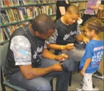  ?? STAFF PHOTOS BY TIFFANY WATSON ?? Southern Maryland Blue Crabs players Norberto Susini and Robert Carson autograph a Blue Crabs baseball hat for Azariah Vinson, 5, a student at James Ryder Randell Elementary School in Clinton.