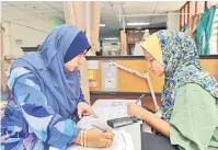  ?? — Gambar Bernama ?? TEKUN MENJAWAB: Guru pengawas peperiksaa­n Nur Suliani Md Ghani membantu murid SK Maras, Nur Ain menulis jawapan pada kertas soalan Bahasa Melayu UPSR di HSNZ di Kuala Terengganu, semalam.