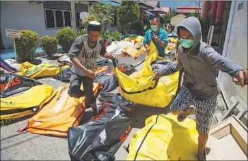  ?? Bay Ismoyo AFP/Getty Images ?? FAMILY MEMBERS carry away one of those killed in Palu, where crumpled buildings and bridges were surrounded by bodies. “Many families are in urgent need of help,” said one humanitari­an aid worker.