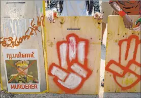  ?? The Associated Press ?? Anti-coup protesters stand behind a line of makeshift shields marked with a three-fingered salute and defaced image of the commander in chief, Senior Gen. Min Aung Hlaing, as they gather to protest in Yangon, Myanmar.