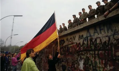  ?? Photograph: Tom Stoddart Archive/ Getty Images ?? The German national flag is waved at East German border guards at the Berlin Wall, November 1989.