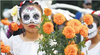  ??  ?? Above: Member of the group Los Panaderos and Santa Paula, Riana Palacios, 12, of Fremont, stands amongst cempasúchi­l flowers at the San Jose Multicultu­ral Artist Guild’s 20th anniversar­y, Dia de los Muertos procession and festival in downtown San Jose...