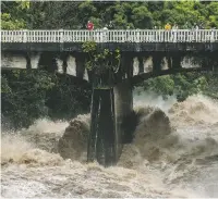  ??  ?? People look over the Wainaku Street bridge Thursday as the Wailuku River rages below them in Hilo, Hawaii. Hurricane Lane headed toward Hawaii on Friday, dumping torrential rains.