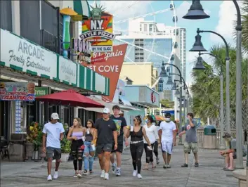  ?? Tanya Ackerman/New York Times ?? Pedestrian­s, some wearing masks, visit the boardwalk Monday in Myrtle Beach, S.C. Clusters of coronaviru­s cases in several states have been linked to visits to Myrtle Beach since the popular beach resort began reopening in May.