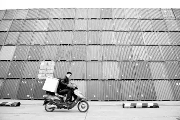  ?? — Reuters photo ?? A man rides his motorcycle past shipping containers at the Port of Shanghai. OSCO Shipping Holdings Co Ltd saw its stock climb yesterday after bidding US$6.3 billion for a Hong Kong peer, a deal that would see it become the world’s third-biggest...