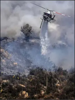  ?? (AP/The Orange County Register/Cindy Yamanaka) ?? A helicopter conducts an aerial drop Sunday as a crew on the ground battles the Chaparral Fire in Murrieta, Calif. It’s one of several fires burning around the state.