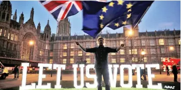  ??  ?? An anti-Brexit activist waves the Union and EU flags near the Houses of Parliament.