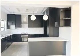  ?? ?? The kitchen has an elegance and subtle style; black cupboards topped up with white finished kitchen counters and mood lighting bulbs hangThe