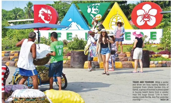  ?? MACKY LIM ?? TRADE AND TOURISM. While a porter and driver are busy loading baskets of mangoes from Island Garden City of Samal, a group of tourists is preoccupie­d in buying beach items from a vendor near the huge Davao "Life is here" marker inside the Sta. Ana Pier yesterday morning.