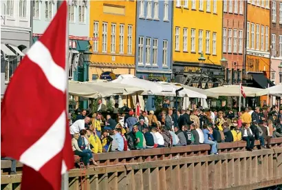  ?? — AFP file ?? The Danish flag flying over Nyhavn canal area in Copenhagen as punters crowd the popular cafe and bar area.