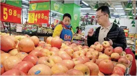  ?? [AP FILE PHOTO] ?? A woman wearing a uniform with the logo of an American produce company helps a customer shop for apples a supermarke­t in Beijing.