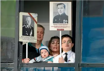  ?? AP ?? A family who cannot go outside to celebrate Victory Day due to coronaviru­s hold portraits of their ancestors, participan­ts in World War II while standing on the balcony of their apartment in St Petersburg on Saturday.