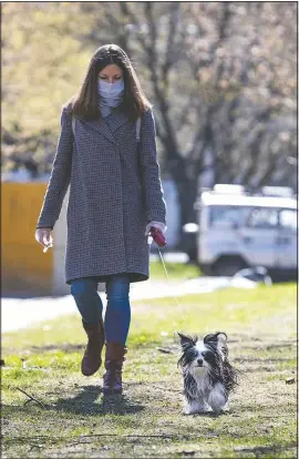  ??  ?? Volunteer Nadezhda Minyaeva, wearing a face mask and gloves to protect from coronaviru­s, walks Margarita Donchenko’s dog April 27 in a courtyard outside of the apartment building in Moscow.