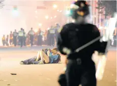  ?? RICH LAM/GETTY IMAGES ?? Riot police walk in the street as a couple kiss on June 15, 2011 in Vancouver. The city broke out in riots when the Canucks lost Game 7 of the Stanley Cup Final.