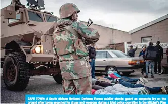  ?? —AFP ?? CAPE TOWN: A South African National Defense Forces soldier stands guard as suspects lay on the ground after being searched for drugs and weapons during a joint police operation in the Mitchel’s Plan district of the Cape Flat in Cape Town.