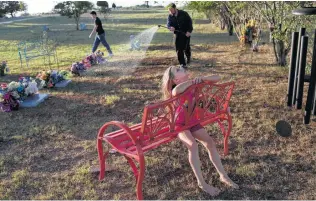  ?? Photos by Lisa Krantz / Staff photograph­er ?? John Holcombe, with his children, Evelyn Hill, 8, and Philip Hill, 16, waters flowers and an olive tree they planted at the graves of nine family members who are buried in Sutherland Springs.