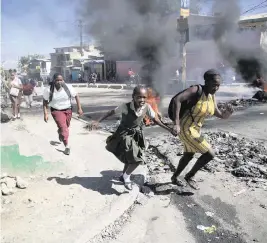  ?? ODELYN JOSEPH AP ?? A woman and her daughter move past a barricade that was set up by supposed police officers who were protesting in Port-au-Prince, Haiti, on Thursday.