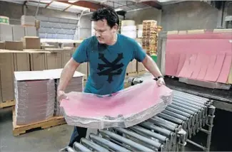  ??  ?? ALFREDO PAREDES loads pink doughnut boxes from a shrink wrap machine manufactur­ed at Evergreen Packaging in La Mirada. Pink boxes are a few cents cheaper than white ones.