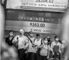  ?? AGENCE FRANCE PRESSE ?? People stand in front of an electronic display showing the Hang Seng Index in the Central district of Hong Kong on July 26, 2021, after stocks plunged as tuition firms were hammered by China's decision to reform the private education sector by preventing them from making profits.