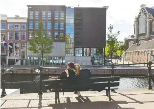  ??  ?? A couple sits across from the empty Anne Frank House in Amsterdam’s deserted city centre.