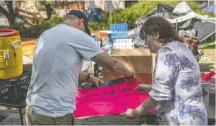  ?? ?? Breann Dow, right, a volunteer at the makeshift encampment at city hall for those experienci­ng homelessne­ss, prepares a sign intended to help lift the spirits of the residents, many of whom struggle with addictions.