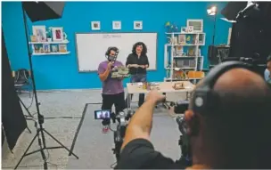  ??  ?? A cameraman gives directions to teacher Rania Koukli as she prepares to record lessons broadcast on public television at an elementary school in Athens. State television is making and broadcasti­ng lessons, while teachers sit in empty classrooms talking to remote students. Despite some problems, they say it keeps children in touch with their schools.