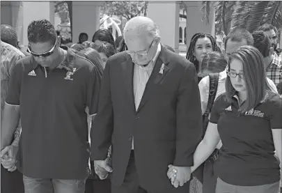  ?? Associated Press ?? ■ Florida Internatio­nal University President Mark B. Rosenberg, center, joins hands with baseball coach Mervyl Melendez, left, and student government president Krista Schmidt as they bow their heads during a moment of silence Monday in Miami for the...