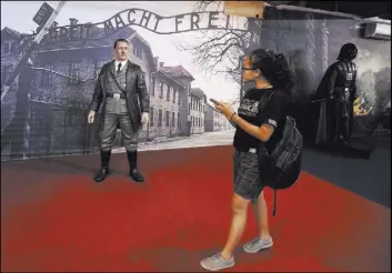  ?? Slamet Riyadi The Associated Press ?? A visitor at De Mata Museum in Yogyakarta, Indonesia, walks by the figure of Adolf Hitler displayed Wednesday against the backdrop of an image of Auschwitz-Birkenau.