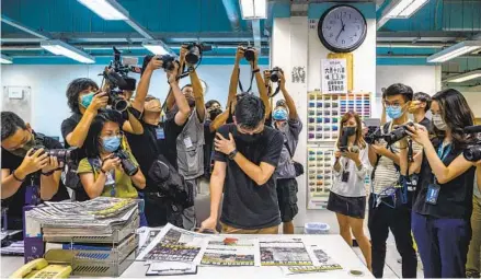  ?? ANTHONY WALLACE AFP VIA GETTY IMAGES ?? Journalist­s take photos as an Apple Daily employee proofreads the newspaper before it goes to print in Hong Kong on Thursday, after police raided its newsroom and arrested the chief editor and four executives of the pro-democracy newspaper that morning.