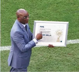  ?? (Reuters) ?? Former Cameroon player Roger Milla holds an award on the pitch with the oldest goal scorer award in World Cup history before the Switzerlan­d-Cameroon match yesterday.