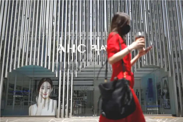  ??  ?? A woman holding her mobile phone walks past an AHC cosmetic store. — Reuters photo