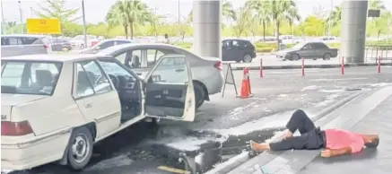  ??  ?? The taxi driver lying down on the pavement after ramming his car into a vehicle at Kota Kinabalu Internatio­nal Airport on Monday.