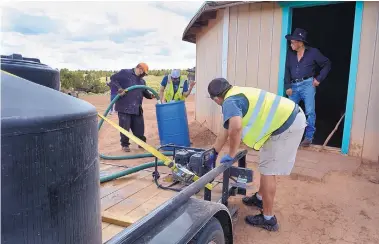  ?? JIM THOMPSON/JOURNAL ?? Steward Barton of Water Warriors United runs the pump as Vernell Tsosie and Anthony Francis of the St. Francis Chapter House fill up a water barrel for resident Robert Wilson.