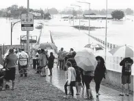  ?? Rick Rycroft / Associated Press ?? People shelter under umbrellas Monday as they watch the flooded Hawkesbury River in Windsor, northwest of Sydney, Australia. Hundreds of people have been rescued from floodwater­s.