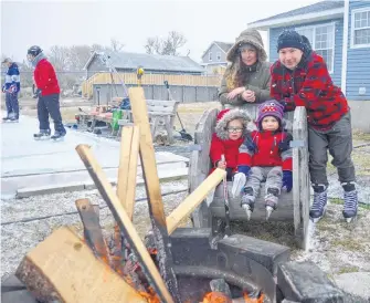  ?? DAVID JALA/CAPE BRETON POST ?? Three-year-old twins Riley, left, and Reese Scott, along with parents Deena and Mark, take a break by the fire pit after spending some time on their neighbours’ outdoor rink in Dominion. The 55 ft. by 35 ft. ice surface is located behind the home of Scott McCulloch, wife Melinda Turnbull and son Riley. Recent below-zero temperatur­es have meant great ice conditions and that’s great news for the many friends and family members who have been showing up at the backyard venue that also includes a cosy fire pit.