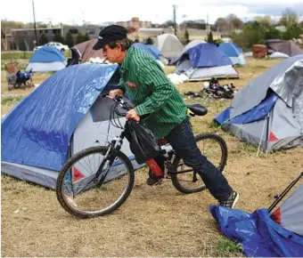  ?? STAFF PHOTO BY DOUG STRICKLAND ?? Chuck Harris climbs onto his bicycle outside his tent in a homeless encampment off East 11th Street on Friday.