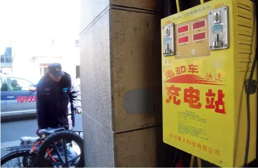  ??  ?? A cyclist has his e-bike charged by using a public e-bike charging facility on the intersecti­on of Weihai Road and Maoming Road N. in Shanghai. — Dong Jun