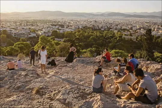  ?? EIRINI VOURLOUMIS PHOTOS / THE NEW YORK TIMES ?? Tourists sit under the Parthenon and watch the sunset Aug. 13 over Athens, Greece. After visiting the Acropolis, thousands of tourists board hulking ferryboats for vacations on the sunny Greek islands. Tourism has been surging, helping reinvigora­te growth after years of sharp spending cuts and tax hikes.