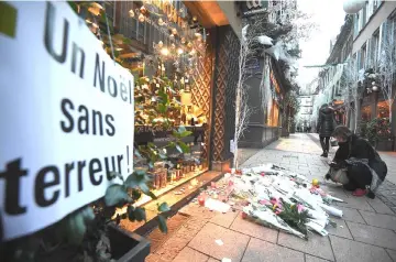  ?? — AFP photo ?? A woman lights a candle in the street next to a message reading ‘a Christmas without terror’ in tribute to the victims of a deadly shooting two days ago, in central Strasbourg.