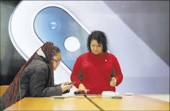  ?? Mary Altaffer The Associated Press ?? An image of an iPhone is on display in the background as a customer, left, gets help at an Apple store in Brooklyn, N.Y., on Thursday. Apple, citing waning demand for its iPhones, warned that revenue for the last quarter of 2018 will fall well below projection­s.